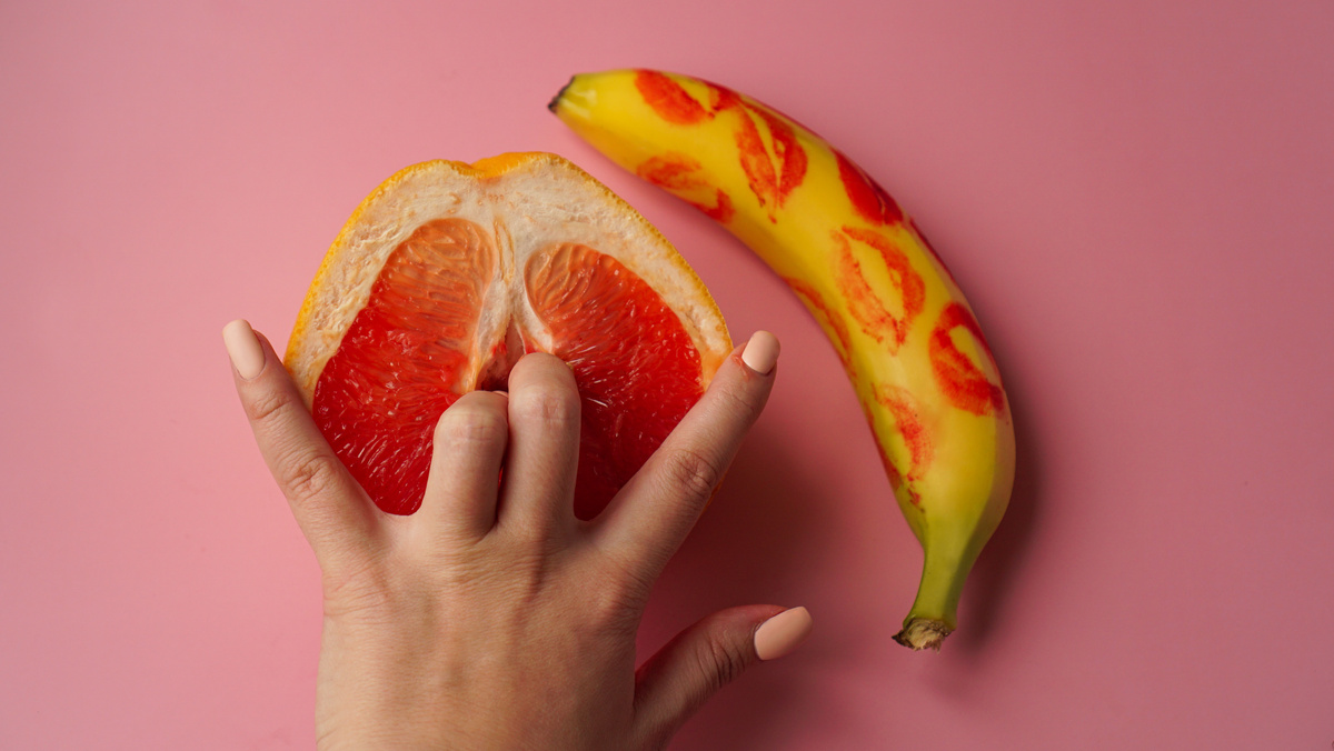 Fingers in grapefruit on pink background. Sex concept.